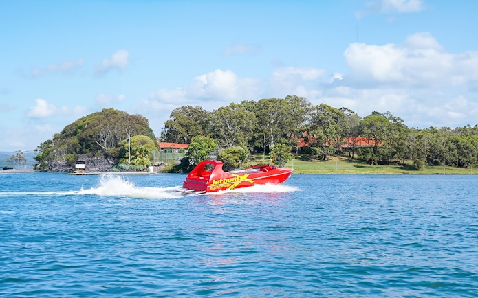 Red jet boat speeding on a blue river with green trees in the background.