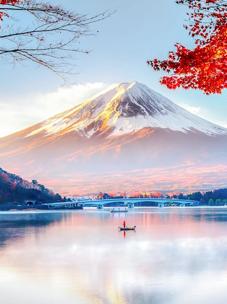 Mount Fuji with red autumn leaves and a boat on Lake Kawaguchi in Japan.