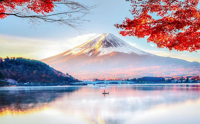 Mount Fuji with red autumn leaves and a boat on Lake Kawaguchi in Japan.