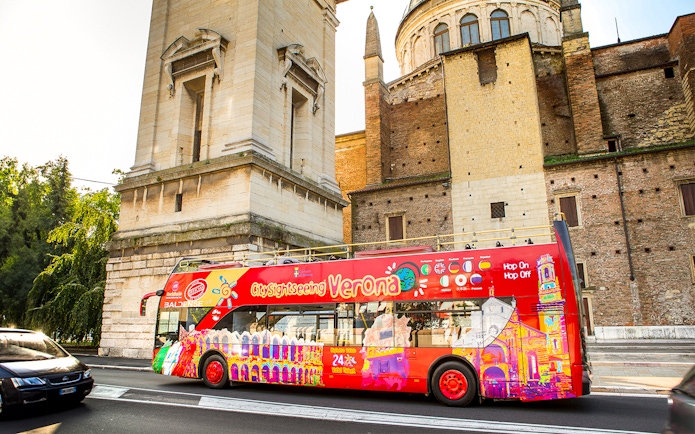 Verona sightseeing bus near historic building on hop-on hop-off tour.