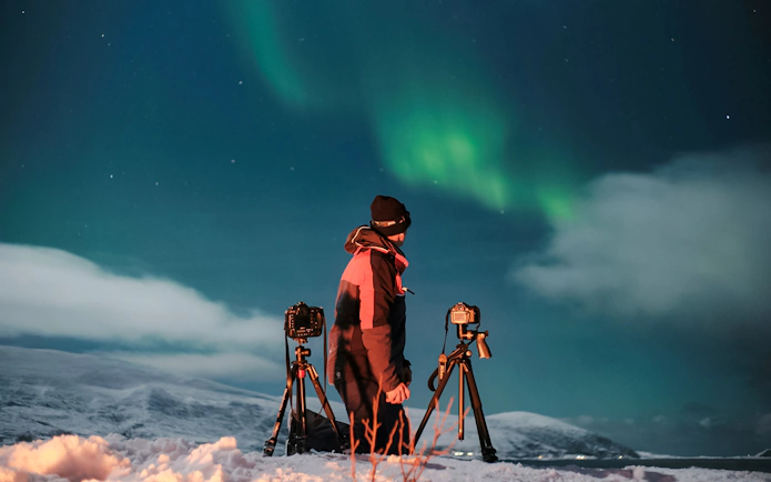 Photographer capturing Northern Lights in Tromsø with cameras on tripods.