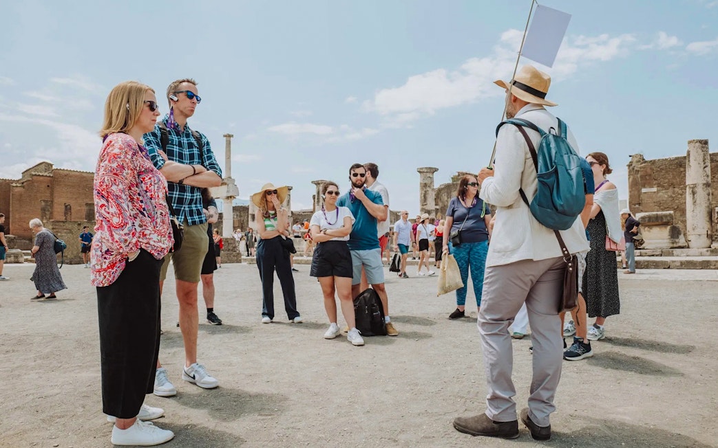 Visitors on a guided tour in Pompeii, standing among ancient ruins.