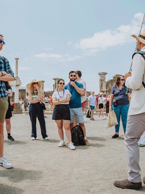 Visitors on a guided tour in Pompeii, standing among ancient ruins.