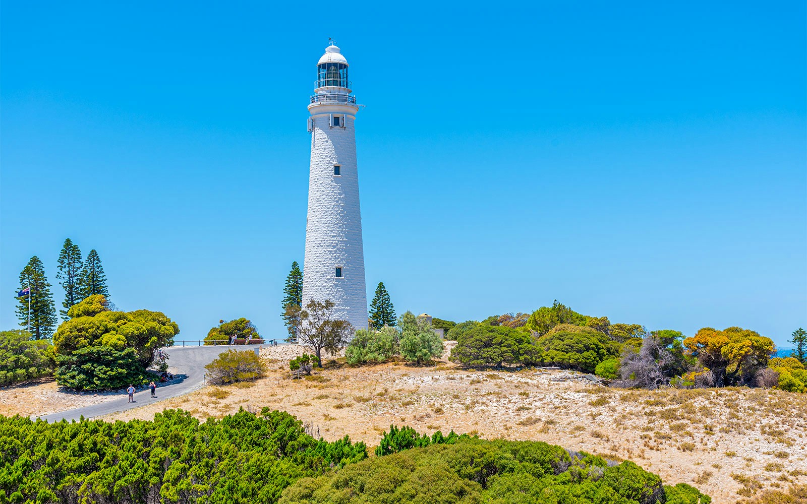 Rottnest Island lighthouse surrounded by trees under a clear blue sky.