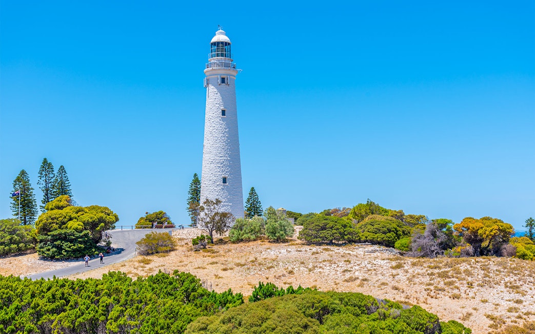 Rottnest Island lighthouse surrounded by trees under a clear blue sky.