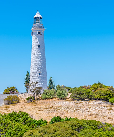 Rottnest Island lighthouse surrounded by trees under a clear blue sky.