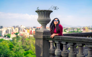 Woman leaning on stone railing at Chapultepec Castle, Mexico City, with cityscape view.