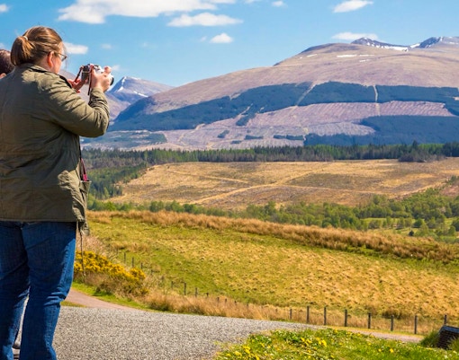 Tourists photographing Loch Ness with mountains in the background, Inverness & The Highlands.