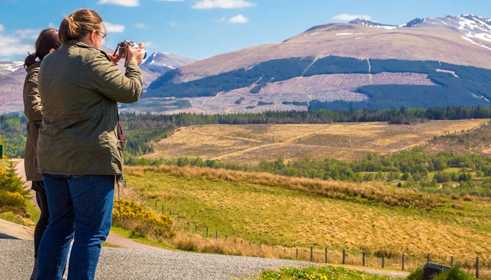 Tourists photographing Loch Ness with mountains in the background, Inverness & The Highlands.