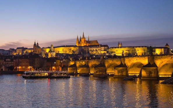 Evening cruise on Vltava River with view of Prague Castle and Charles Bridge.