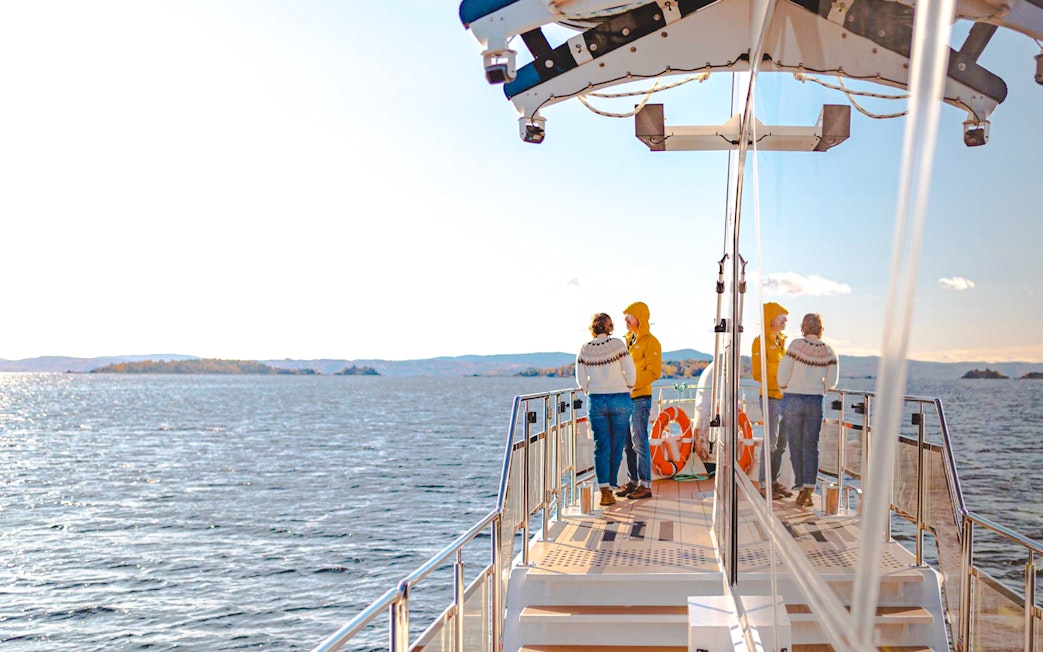 Cruise passengers on deck enjoying Oslo fjord views during a silent sightseeing tour.