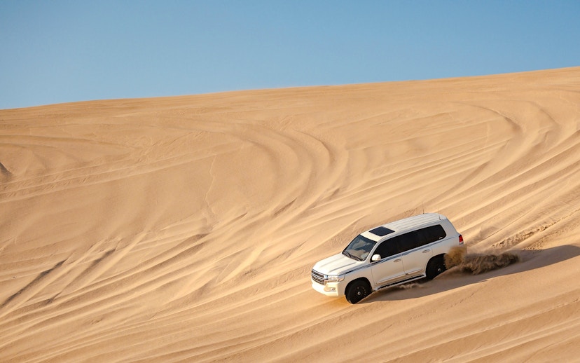 SUV driving on sand dunes during a dune bashing tour in Doha.