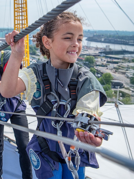 Guests climbing the O2 Arena roof in London during daytime.