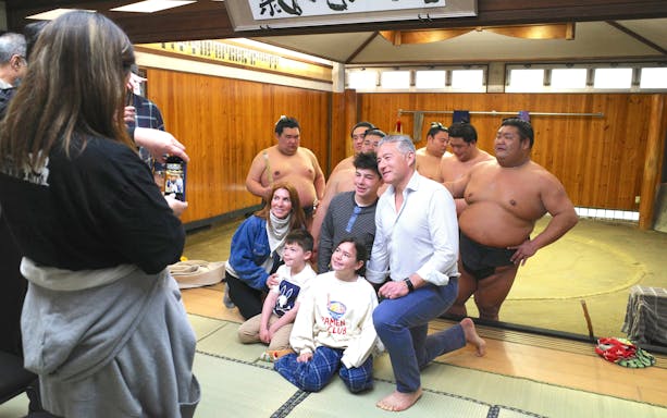 Family posing with sumo wrestlers during morning practice in Asakusa dojo.