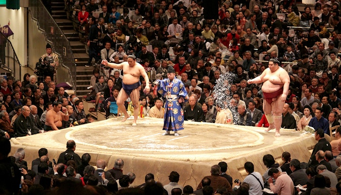 Sumo wrestlers and referee in a tournament ring, Osaka audience watching.