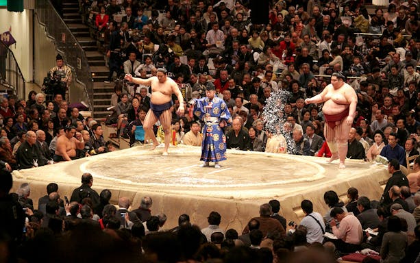 Sumo wrestlers and referee in a tournament ring, Osaka audience watching.