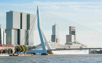 Erasmus Bridge and modern skyline in Rotterdam, featuring a cruise ship docked nearby.