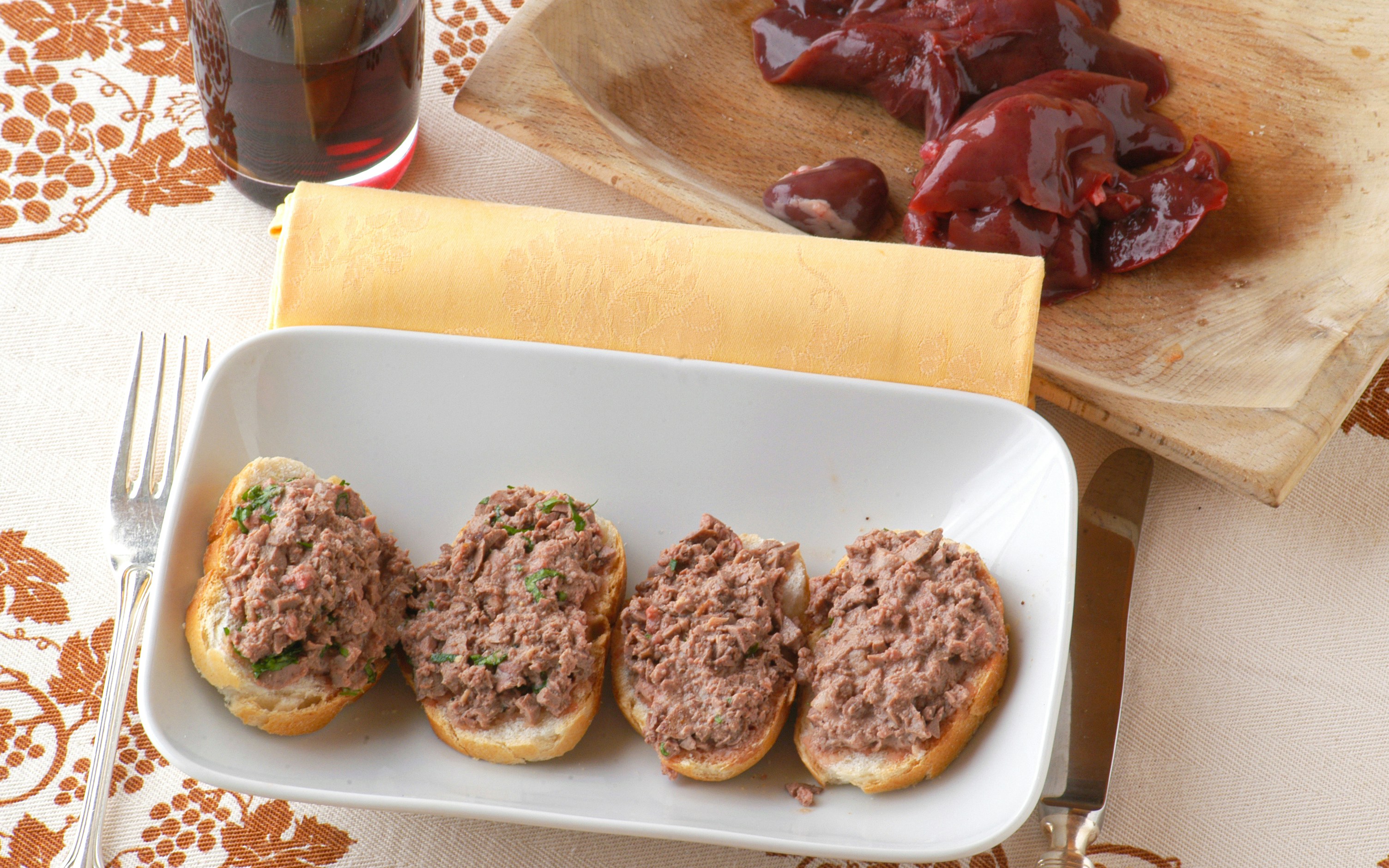 Crostini di fegatini on a plate with liver and a glass of red wine nearby.
