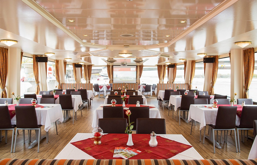 Ein edles Restaurant mit schwarzen Stühlen, weiß-roten Tischdecken und Vorhängen an Deck eines Schiffes