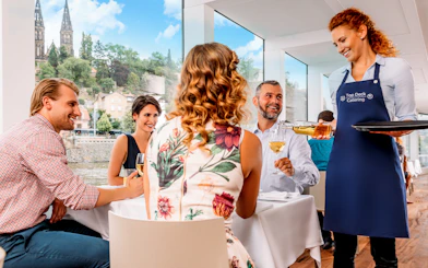 Guests enjoying lunch with wine on a Prague river cruise, with live music and city views.