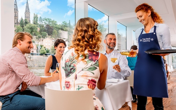 Guests enjoying lunch with wine on a Prague river cruise, with live music and city views.