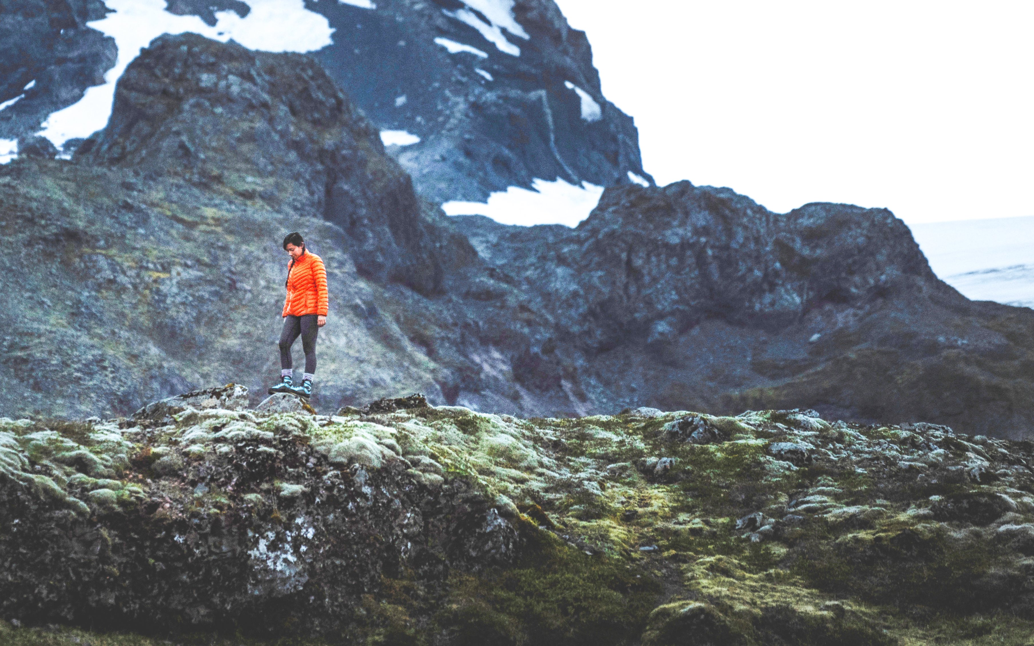 Hiker in orange jacket exploring mossy terrain on the South Coast of Iceland.
