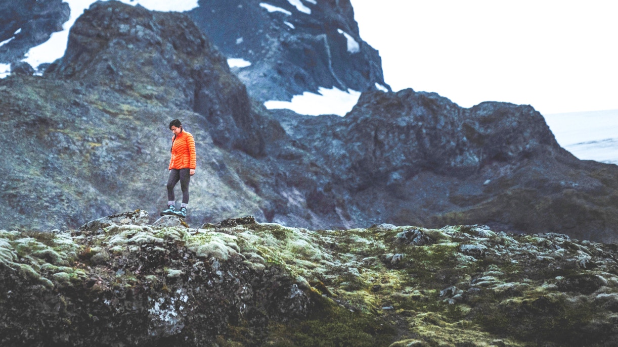 Hiker in orange jacket exploring mossy terrain on the South Coast of Iceland.