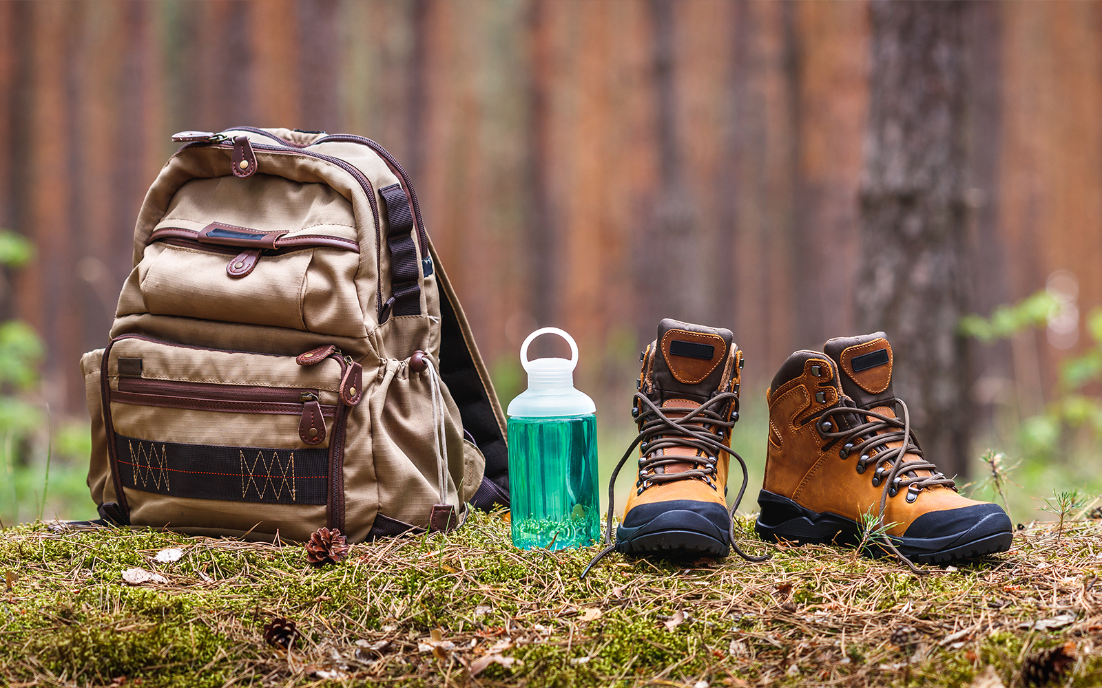 Backpack, water bottle, and leather boots on forest floor for hiking and camping.