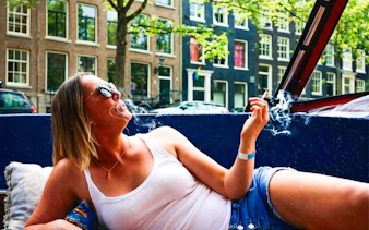 Person relaxing and smoking on a covered boat cruise in Amsterdam canal.