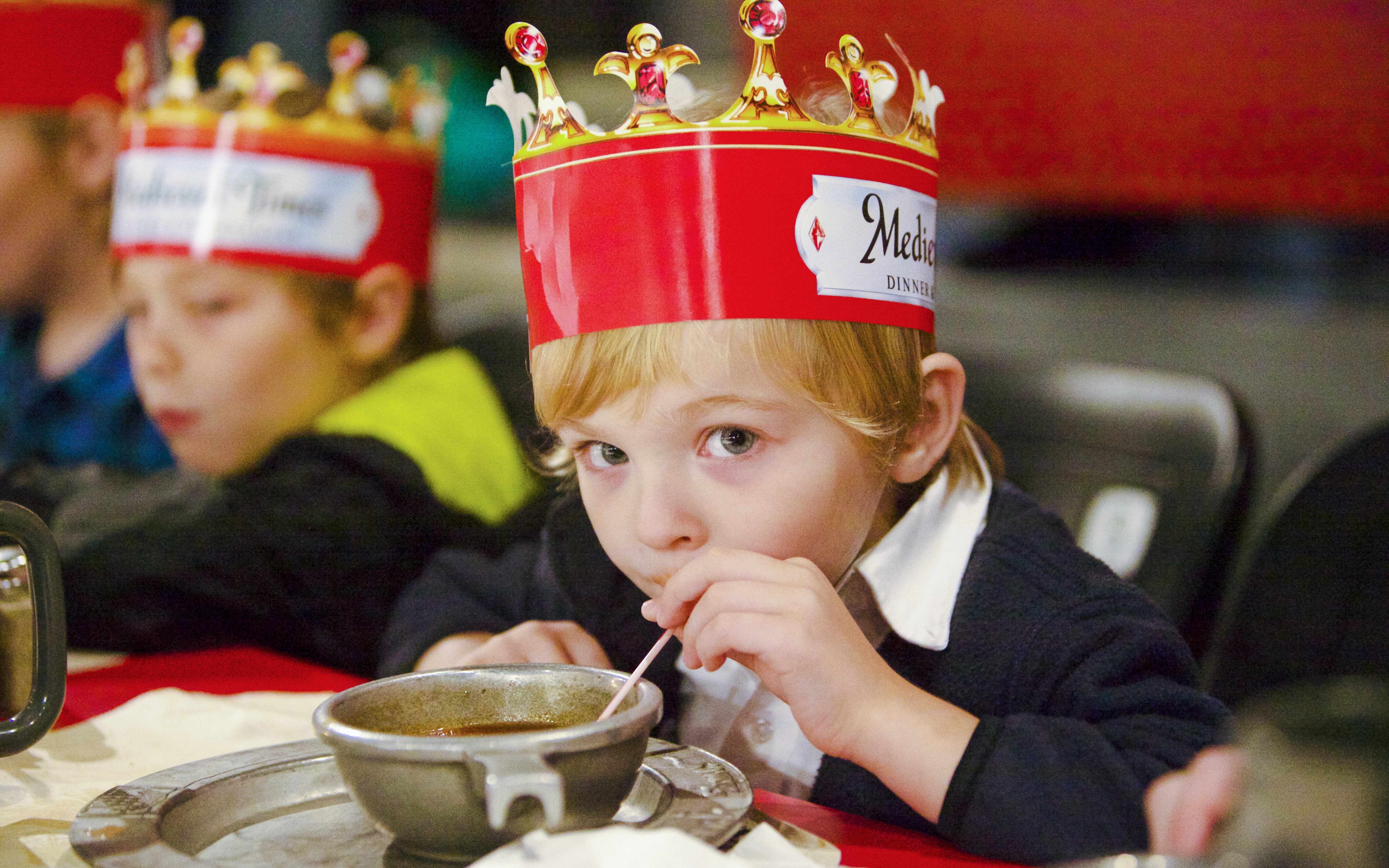 Child enjoying soup at Medieval Times Dinner and Show wearing a crown.