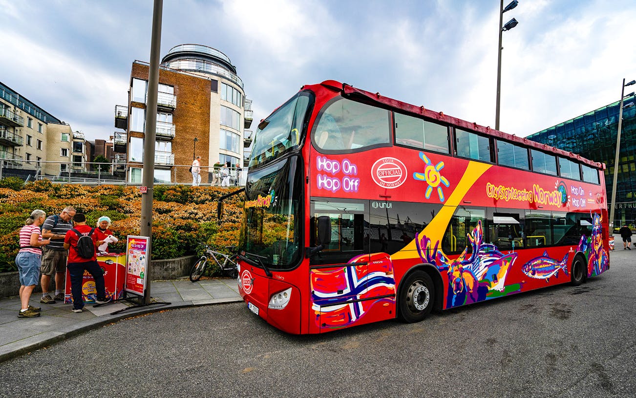 Stavanger hop-on hop-off bus with tourists and city buildings in the background.