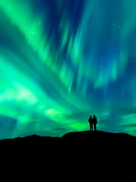 Silhouette of a couple watching the aurora borealis in a clear night sky.