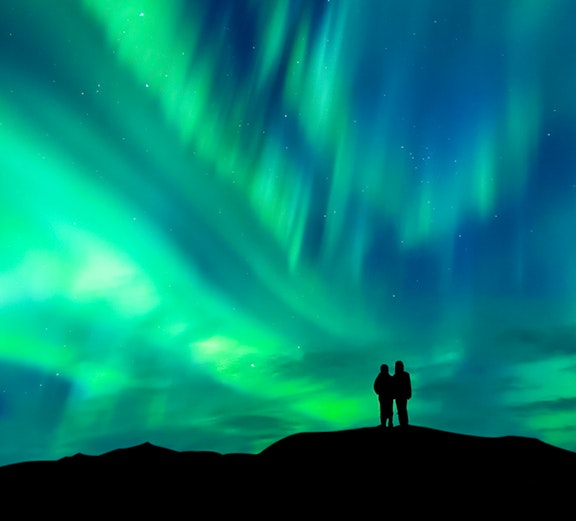 Silhouette of a couple watching the aurora borealis in a clear night sky.
