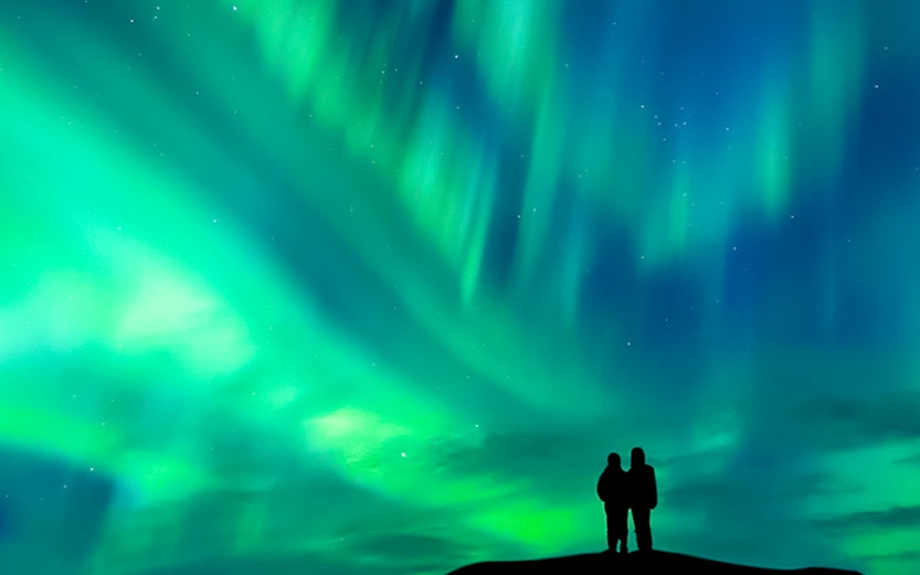 Silhouette of a couple watching the aurora borealis in a clear night sky.