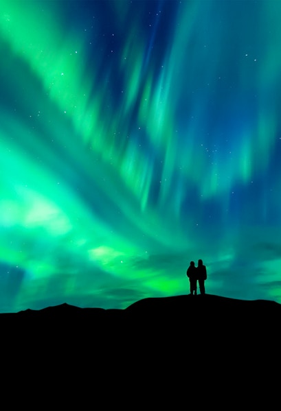 Silhouette of a couple watching the aurora borealis in a clear night sky.