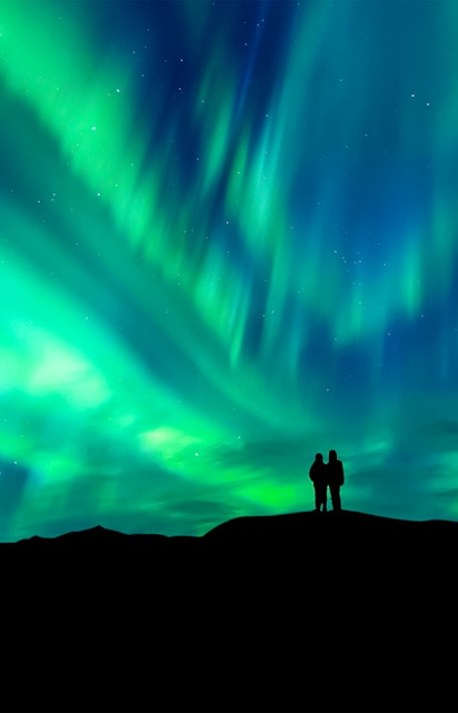 Silhouette of a couple watching the aurora borealis in a clear night sky.