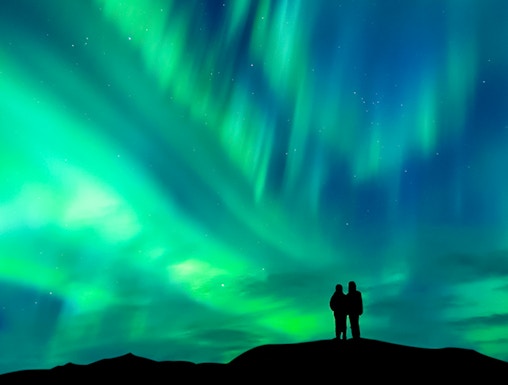Silhouette of a couple watching the aurora borealis in a clear night sky.