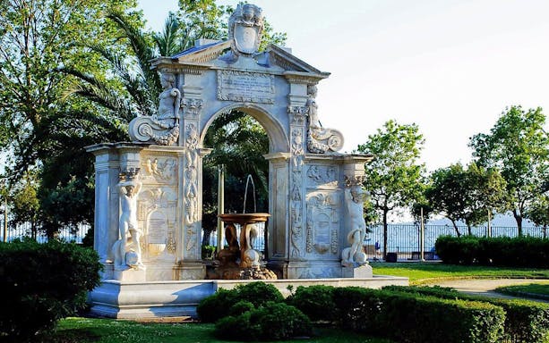 Marble fountain with intricate carvings in a garden setting, Naples tour.