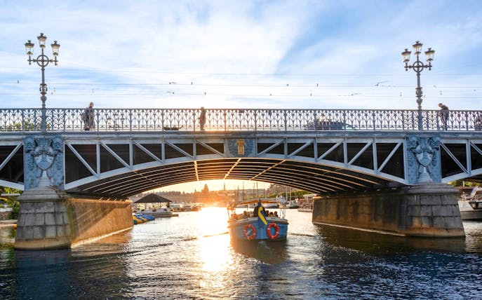 Sightseeing boat tour under Djurgården Bridge in Stockholm at sunset.