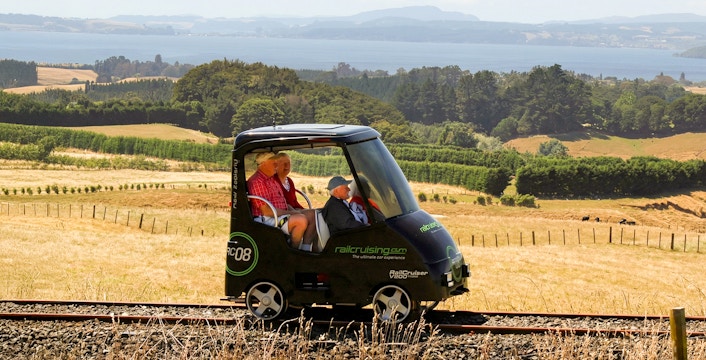 Self-drive rail cart on tracks with scenic Rotorua landscape in the background.