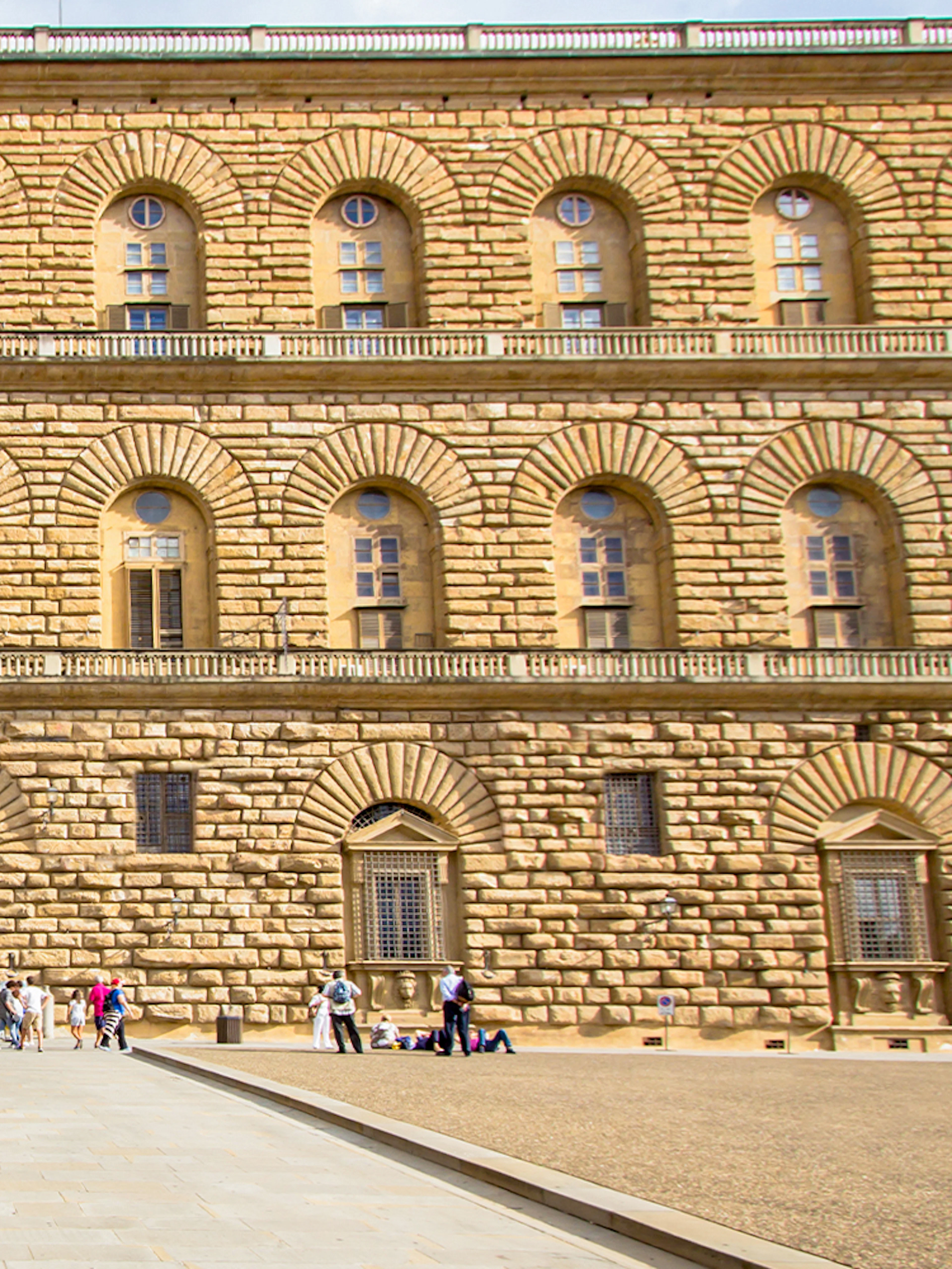 Pitti Palace facade with rusticated stonework in Florence, Italy, featuring arched windows and visitors.