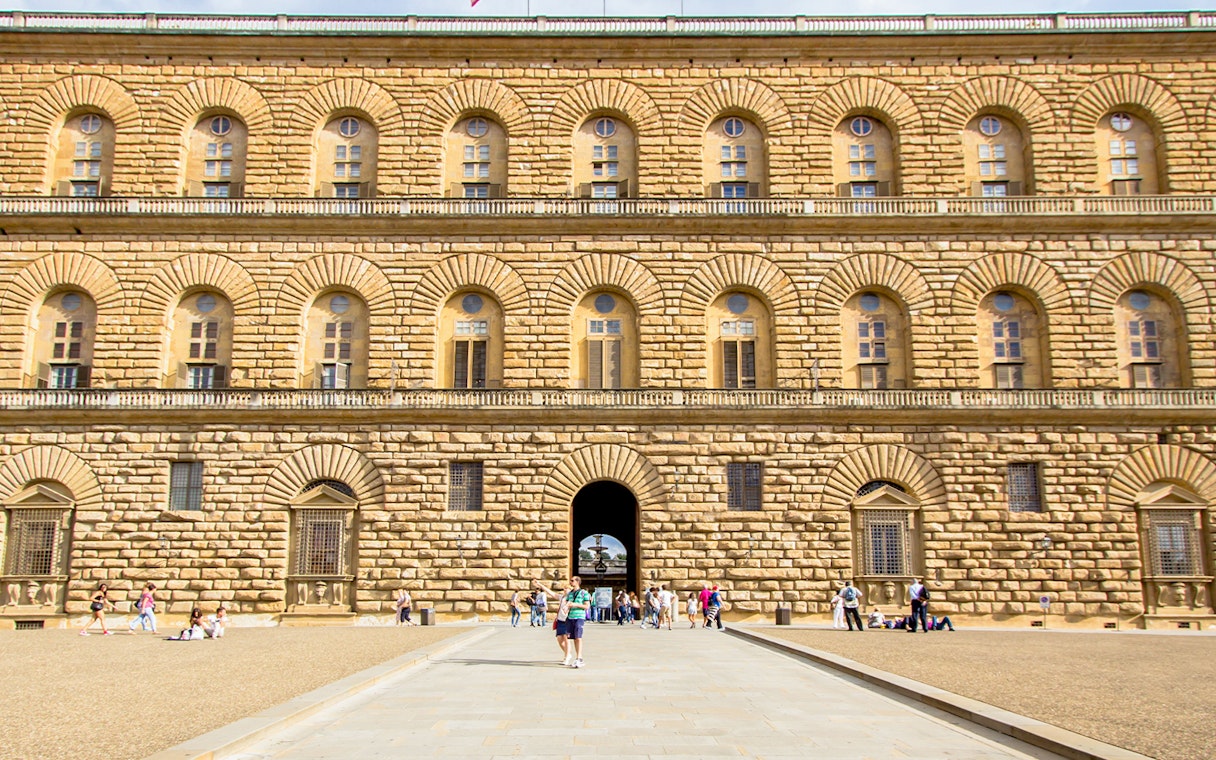 Pitti Palace facade with rusticated stonework in Florence, Italy, featuring arched windows and visitors.