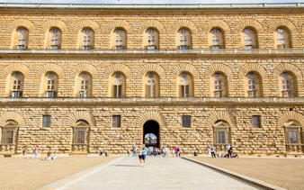 Pitti Palace facade with rusticated stonework in Florence, Italy, featuring arched windows and visitors.