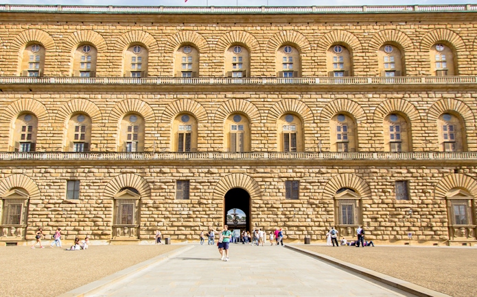 Pitti Palace facade with rusticated stonework in Florence, Italy, featuring arched windows and visitors.