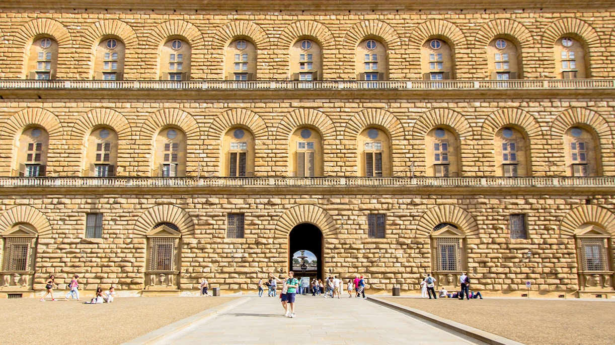 Pitti Palace facade with rusticated stonework in Florence, Italy, featuring arched windows and visitors.