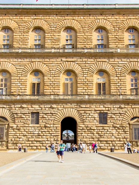 Pitti Palace facade with rusticated stonework in Florence, Italy, featuring arched windows and visitors.