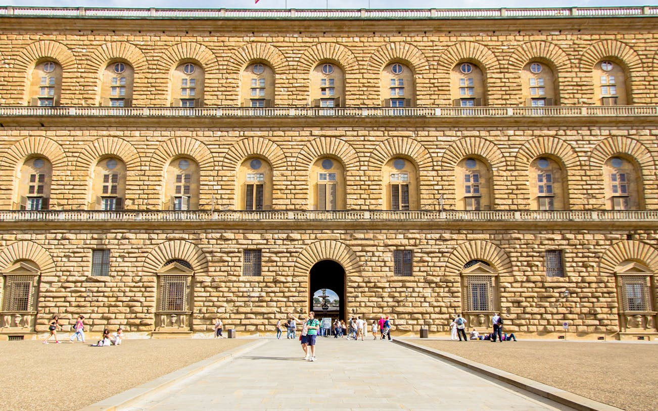 Pitti Palace facade with rusticated stonework in Florence, Italy, featuring arched windows and visitors.