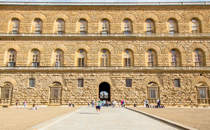 Pitti Palace facade with rusticated stonework in Florence, Italy, featuring arched windows and visitors.