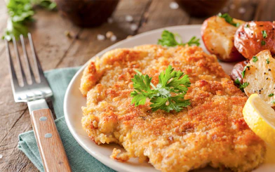 Wiener Schnitzel with roasted potatoes and lemon slice on a plate.