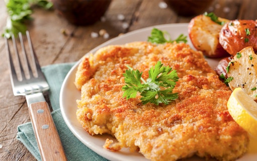Wiener Schnitzel with roasted potatoes and lemon slice on a plate.